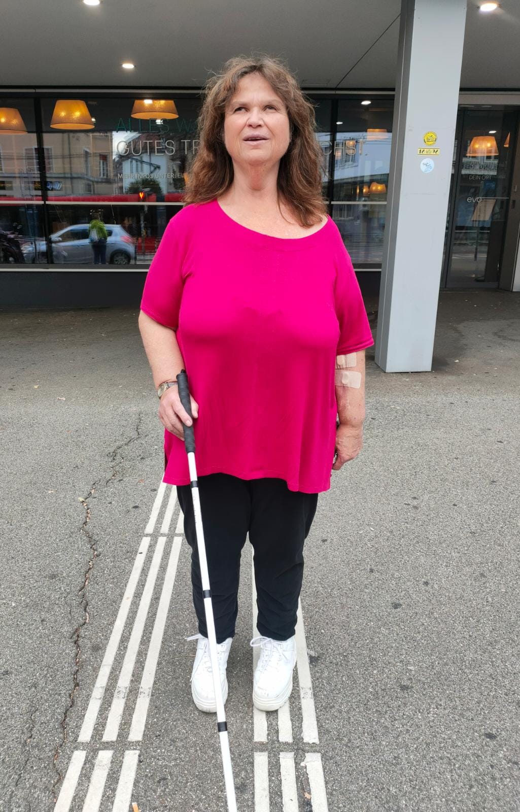 Die stark sehbehinderte Antonella Zanatta vor dem Gebäude an der Effingerstrasse 16. Mit weissem Stock in der Hand auf den Leitlinien für blinde und sehbehinderte Personen stehend